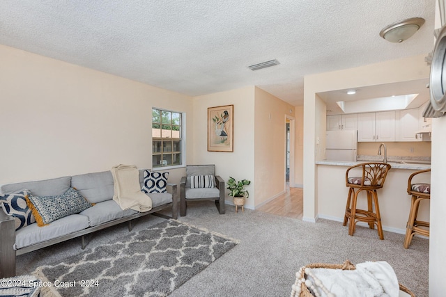 living area with visible vents, light carpet, baseboards, and a textured ceiling