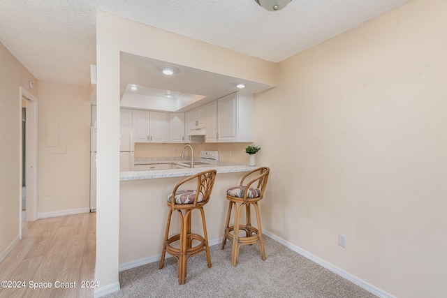 kitchen with white appliances, baseboards, a breakfast bar, light countertops, and under cabinet range hood