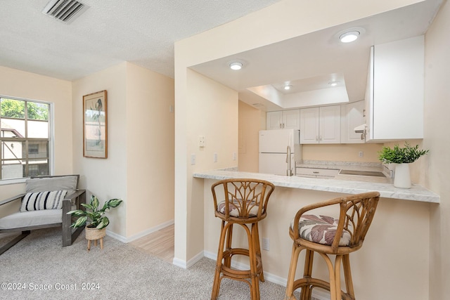 kitchen with light carpet, a breakfast bar, visible vents, light countertops, and freestanding refrigerator