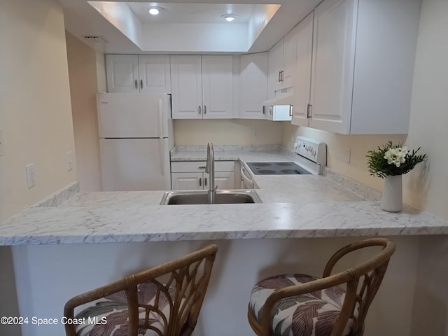 kitchen with white appliances, white cabinets, a breakfast bar, under cabinet range hood, and a sink