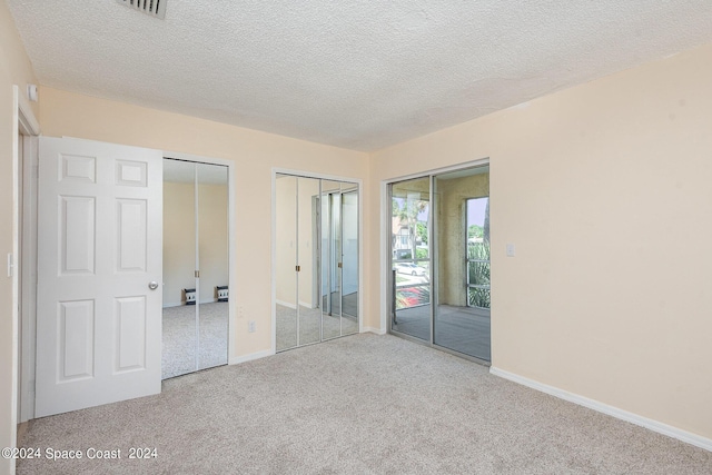 unfurnished bedroom featuring carpet floors, a textured ceiling, baseboards, and multiple closets