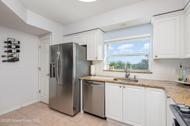 kitchen featuring appliances with stainless steel finishes, a sink, white cabinetry, backsplash, and light tile patterned flooring