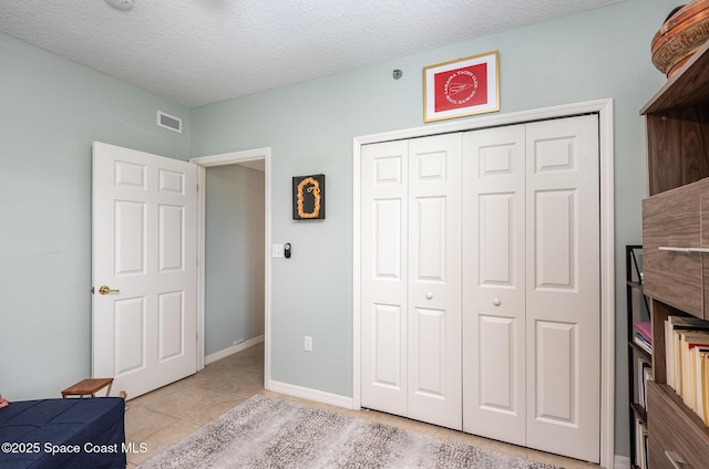 bedroom featuring light tile patterned floors, a closet, visible vents, a textured ceiling, and baseboards