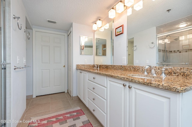 full bath featuring visible vents, tile patterned flooring, a textured ceiling, a shower stall, and a sink