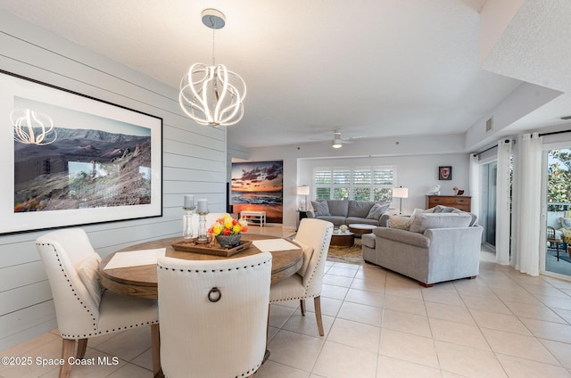 dining space with light tile patterned floors, wooden walls, visible vents, and ceiling fan with notable chandelier