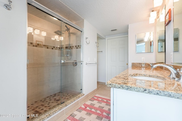 full bathroom featuring a textured ceiling, vanity, visible vents, a shower stall, and tile patterned floors