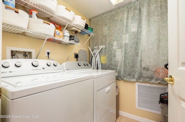 laundry room with washing machine and clothes dryer, light tile patterned floors, visible vents, a textured ceiling, and laundry area