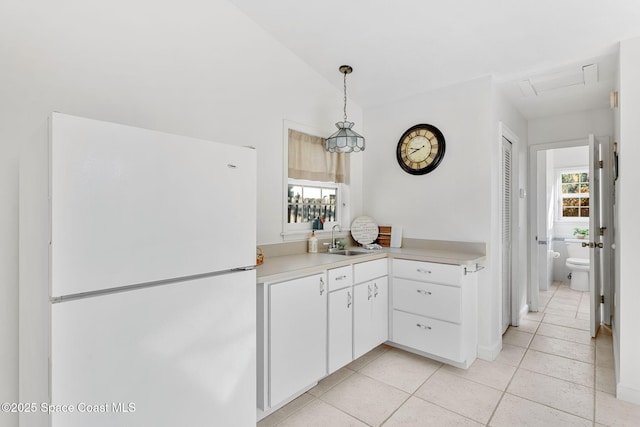 kitchen featuring light countertops, freestanding refrigerator, white cabinetry, a sink, and light tile patterned flooring