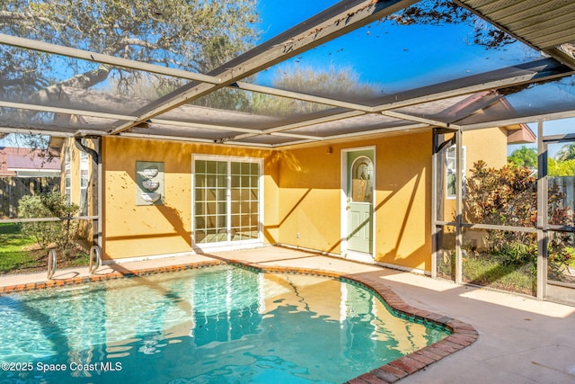 back of property with glass enclosure, a patio, an outdoor pool, and stucco siding