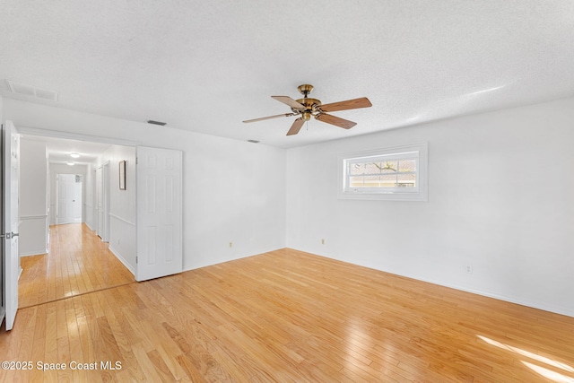 unfurnished room with a textured ceiling, ceiling fan, visible vents, and light wood-style floors