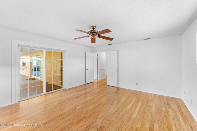 unfurnished room with a textured ceiling, ceiling fan, wood finished floors, and visible vents