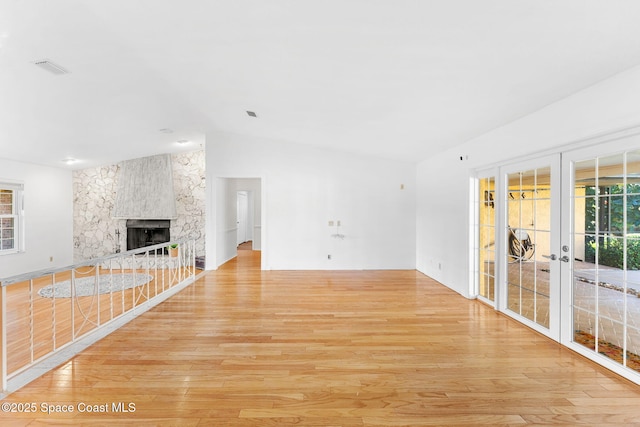 unfurnished living room with light wood finished floors, a fireplace, vaulted ceiling, and french doors