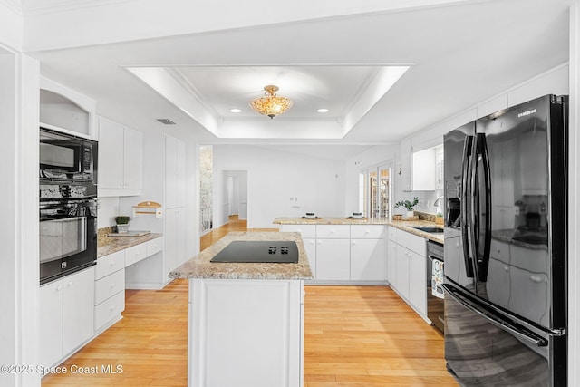 kitchen featuring white cabinets, light wood-style flooring, a peninsula, a tray ceiling, and black appliances