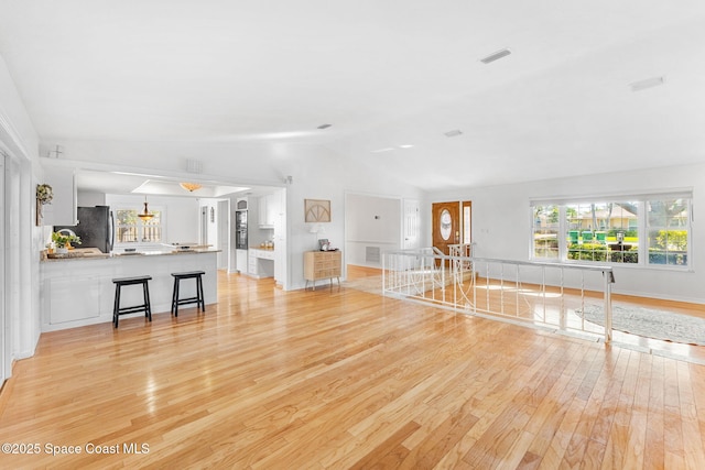 unfurnished living room with lofted ceiling, visible vents, and light wood-style flooring