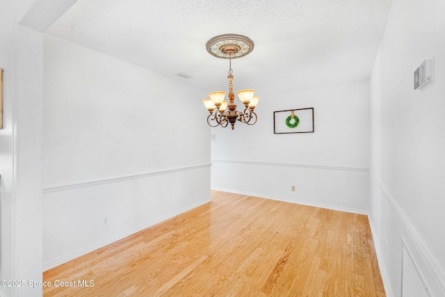 unfurnished room with visible vents, a textured ceiling, wood finished floors, a chandelier, and baseboards