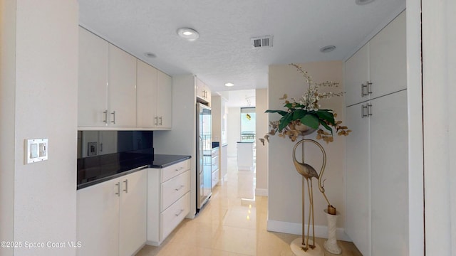 kitchen featuring dark countertops, white cabinetry, visible vents, and a textured ceiling