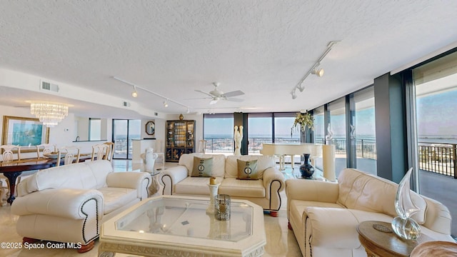 living room featuring a textured ceiling, expansive windows, ceiling fan with notable chandelier, and visible vents