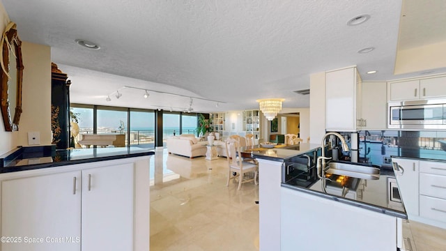 kitchen featuring dark countertops, white cabinets, stainless steel microwave, and a sink