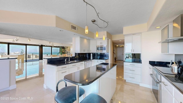 kitchen featuring stainless steel appliances, dark countertops, visible vents, a sink, and a peninsula