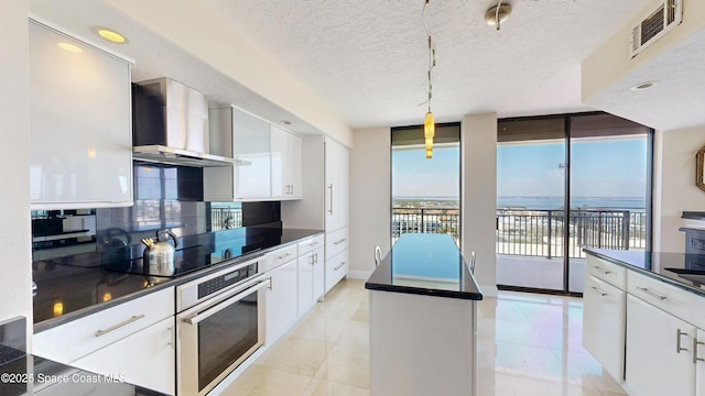 kitchen featuring visible vents, stainless steel oven, wall chimney exhaust hood, tasteful backsplash, and dark countertops