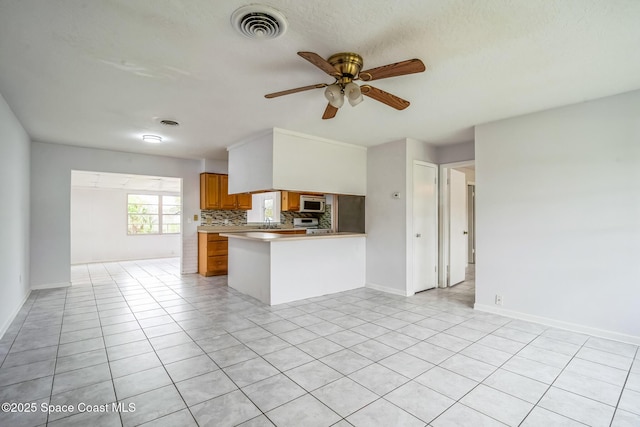 kitchen featuring light tile patterned floors, a peninsula, visible vents, brown cabinets, and decorative backsplash