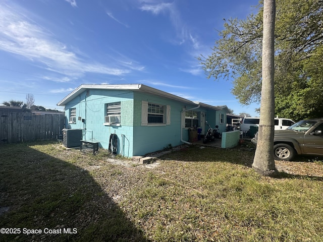 view of side of home with a lawn, fence, cooling unit, concrete block siding, and central AC unit