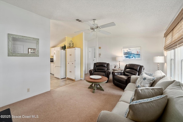 living area with visible vents, a ceiling fan, light colored carpet, vaulted ceiling, and a textured ceiling