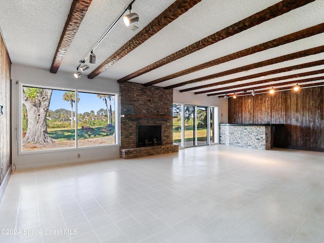 unfurnished living room featuring a fireplace, wood walls, a textured ceiling, track lighting, and beamed ceiling