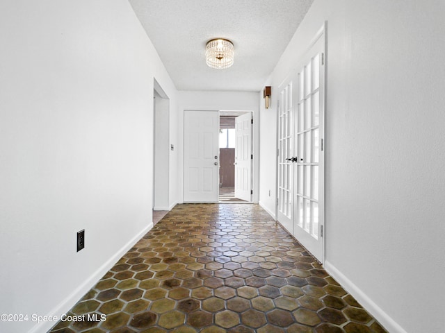 hallway with a textured ceiling, a notable chandelier, and baseboards