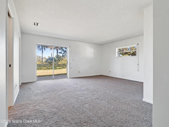 carpeted empty room featuring visible vents, a textured ceiling, and baseboards