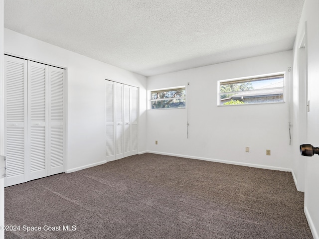 unfurnished bedroom with a textured ceiling, baseboards, multiple closets, and carpet flooring