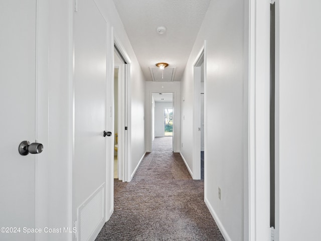 hallway featuring a textured ceiling, carpet flooring, visible vents, baseboards, and attic access