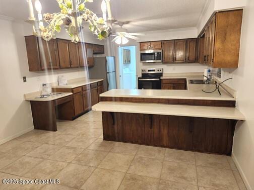 kitchen featuring appliances with stainless steel finishes, a peninsula, light countertops, crown molding, and a sink