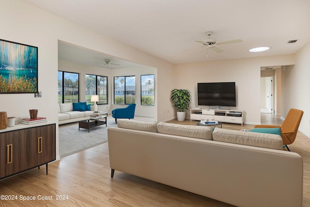 living room featuring ceiling fan, light wood finished floors, visible vents, and baseboards