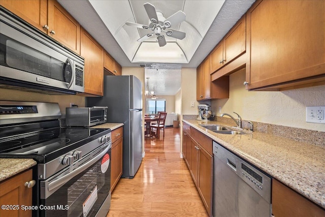 kitchen featuring brown cabinets, appliances with stainless steel finishes, a raised ceiling, and a sink