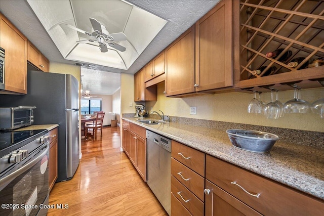 kitchen with a textured ceiling, a sink, appliances with stainless steel finishes, brown cabinets, and light wood finished floors