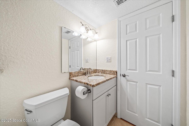 bathroom with toilet, a textured wall, vanity, and visible vents