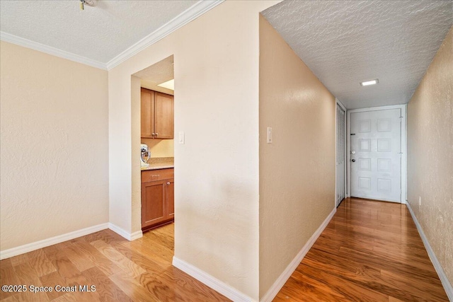 hall with light wood-type flooring, a textured wall, a textured ceiling, and baseboards