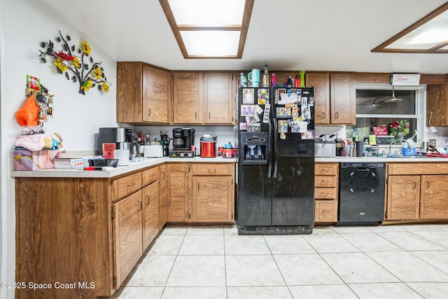 kitchen with brown cabinets, light countertops, black appliances, and light tile patterned flooring