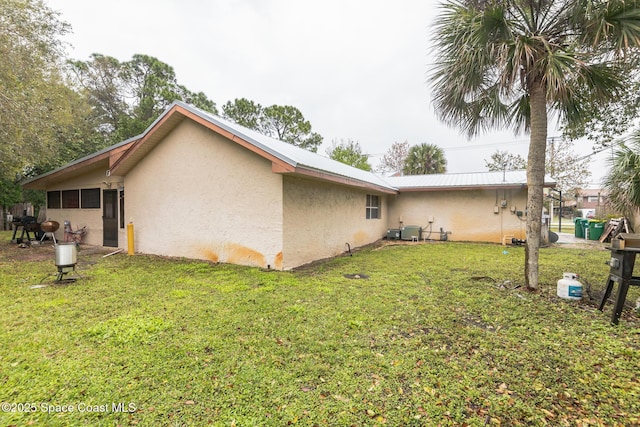 rear view of house featuring a yard, metal roof, central AC, and stucco siding