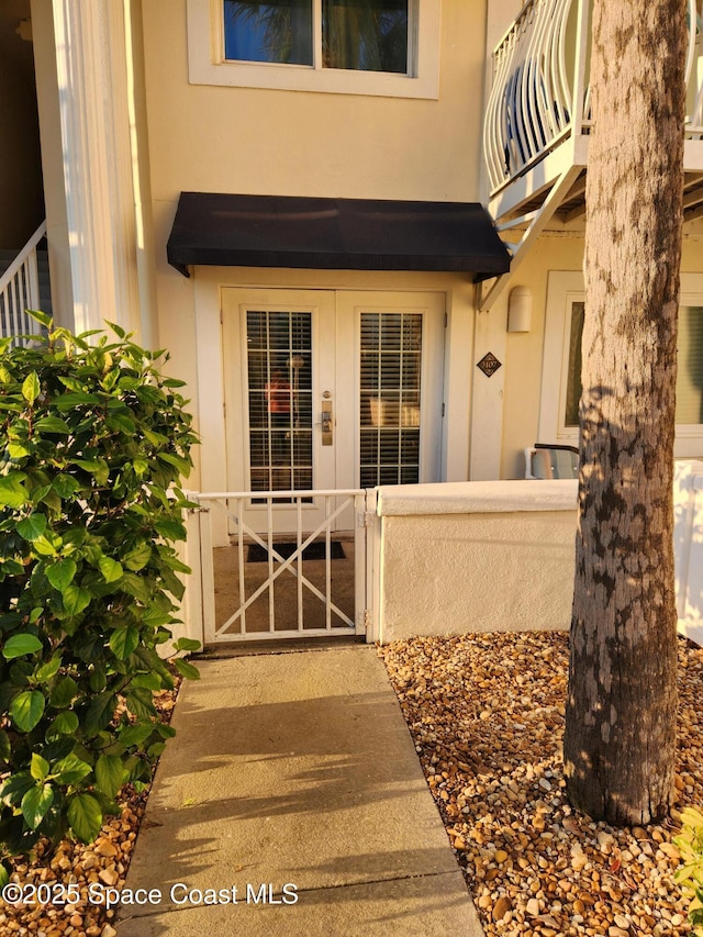 property entrance featuring french doors, a balcony, and stucco siding