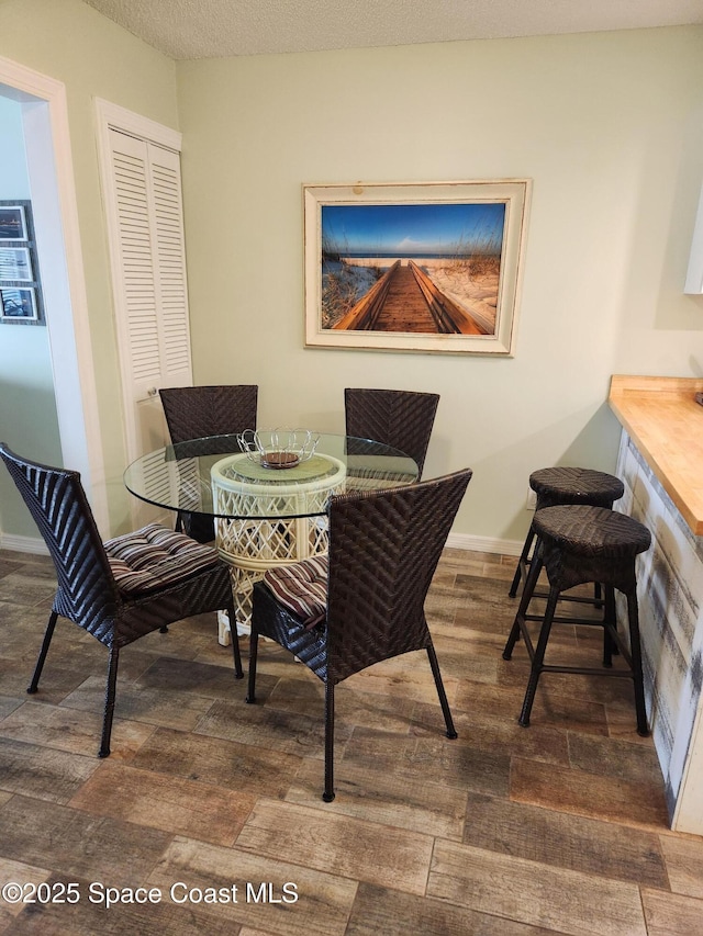 dining area with a textured ceiling, baseboards, and dark wood-style flooring