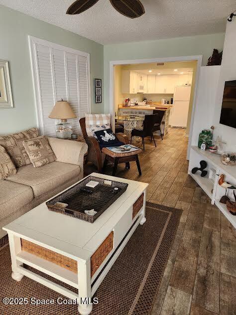 living room featuring a textured ceiling, a ceiling fan, and dark wood-type flooring