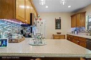 kitchen with light countertops, backsplash, freestanding refrigerator, and brown cabinets