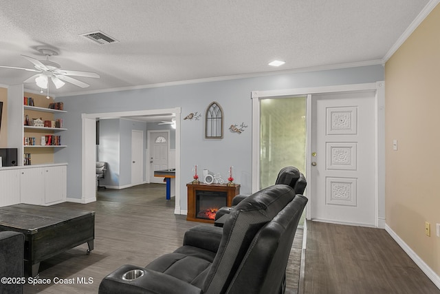 living room with a textured ceiling, ceiling fan, dark wood-type flooring, visible vents, and ornamental molding