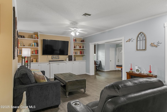 living room with visible vents, a ceiling fan, ornamental molding, wood finished floors, and a textured ceiling