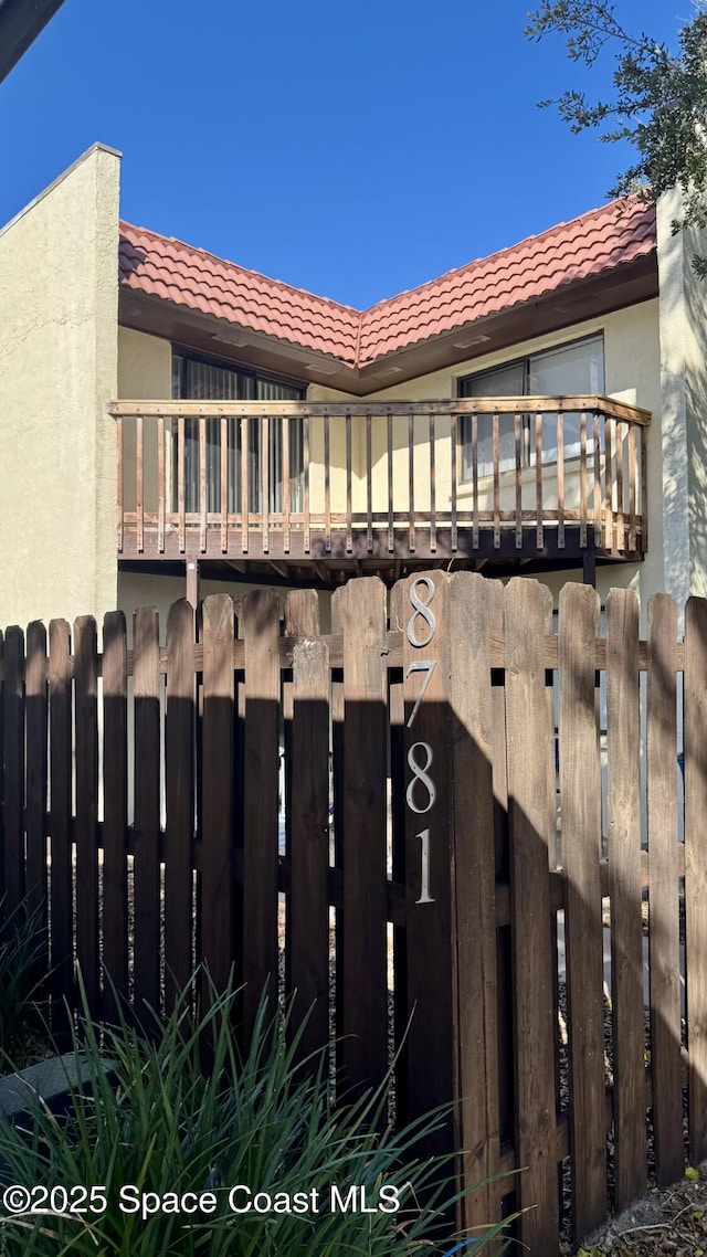 view of side of home featuring fence, a tiled roof, a balcony, and stucco siding