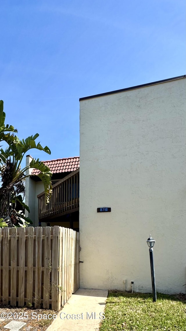 view of side of home featuring a tile roof, fence, and stucco siding