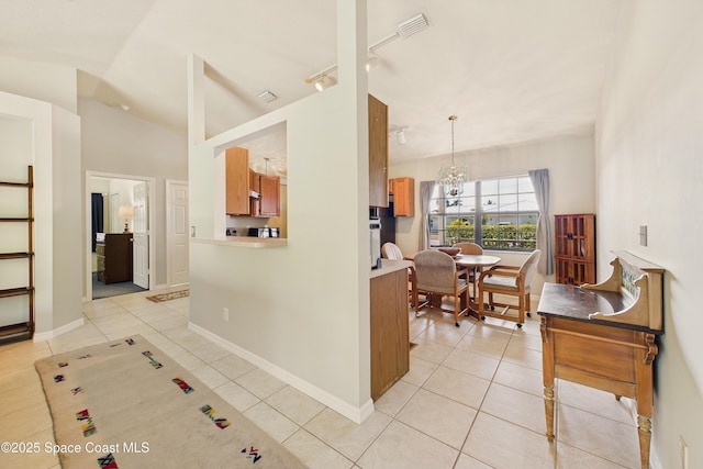 kitchen featuring lofted ceiling, light tile patterned floors, brown cabinetry, rail lighting, and an inviting chandelier