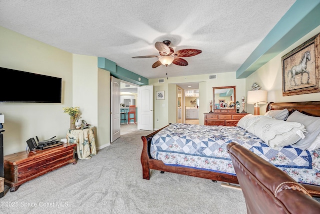 carpeted bedroom featuring a ceiling fan, ensuite bath, visible vents, and a textured ceiling